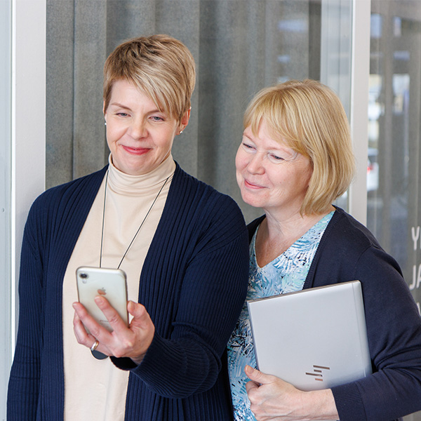 Kaksi naista katsoo kännykkää, jossa esillä Brändin näkyvyyden edistämisen verkkokurssi.
