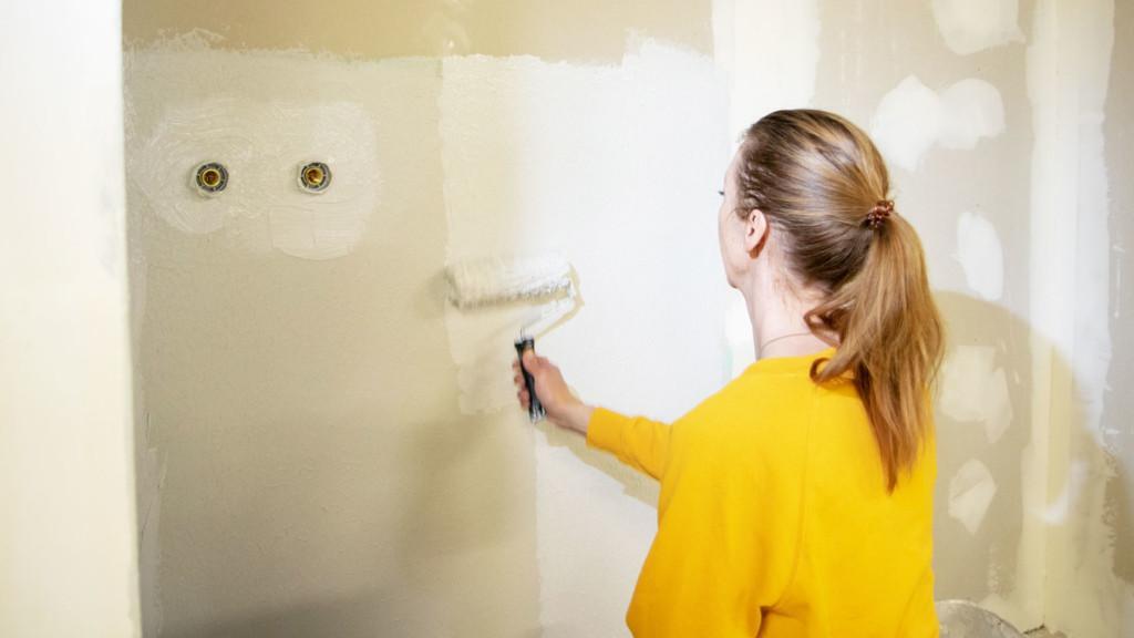 Nainen remontoi seinää, maalaa telalla seinää valkoiseksi.