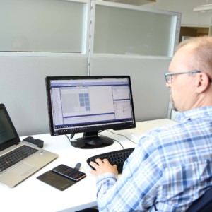 Mies istuu työpöydän ääressä kannettavam tietokoneen edessä ja tekee töitä näppäimistöllä.