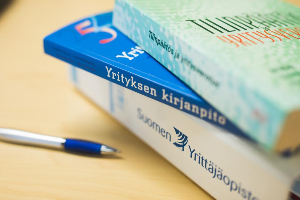 Kirjanpidon ja tilinpäätöksen kirjoja ja Suomen Yrittäjäopiston kansio ja kynä pöydällä.