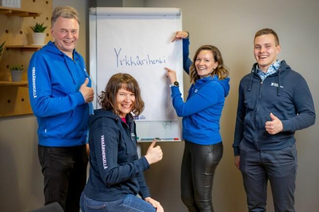 Kuvassa Suomen Yrittäjäopiston työntekijöitä sekä taulu, jossa lukee Yrkkärihenki.