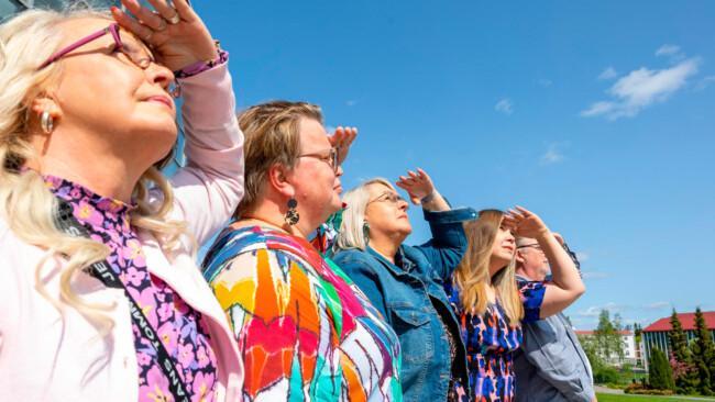 Neljä naista ja yksi mies värikkäissä vaatteissa tähyilee ylöspäin horisonttiin.