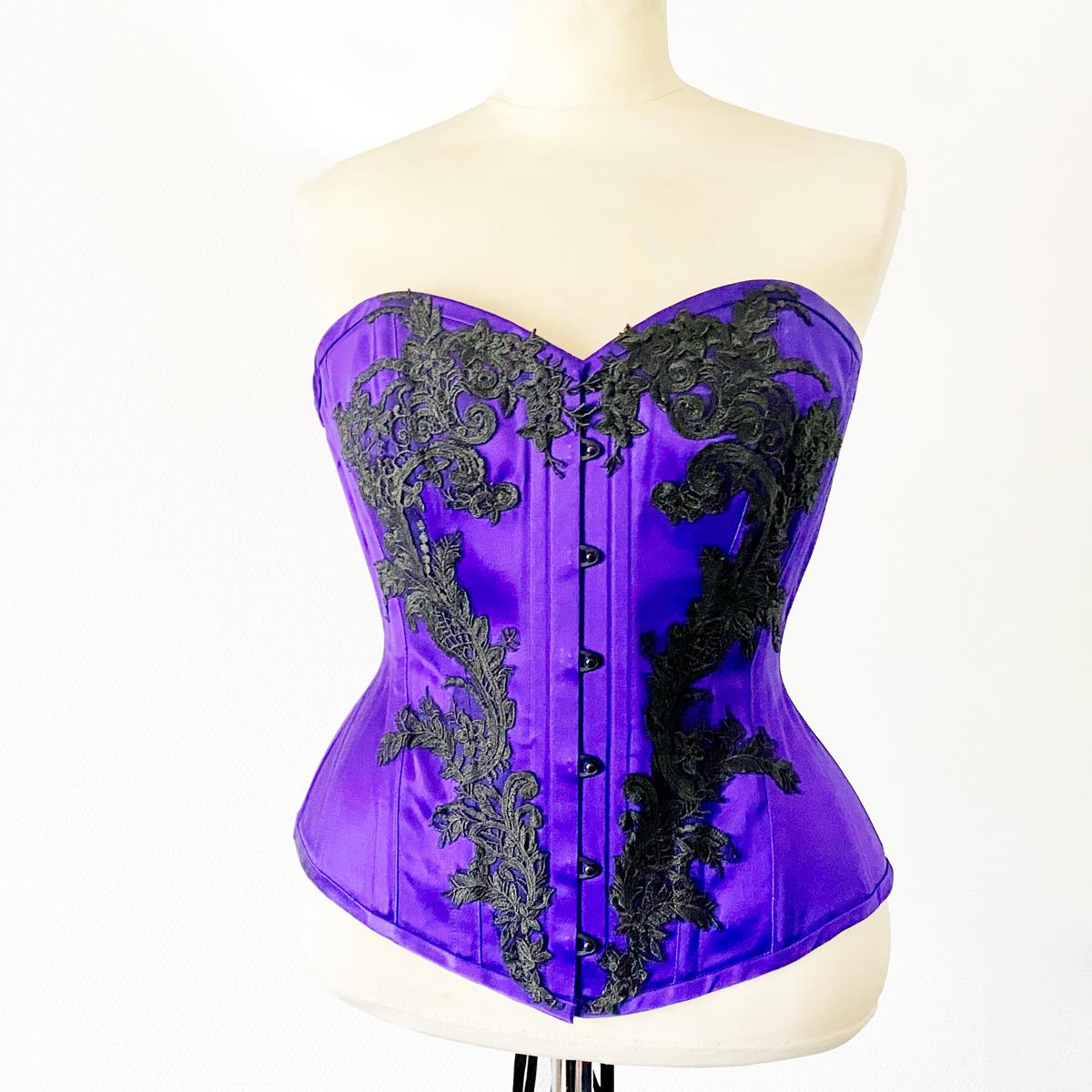 Violetti rinnanylikorsetti, jossa mustia koukeroisia koristeita.