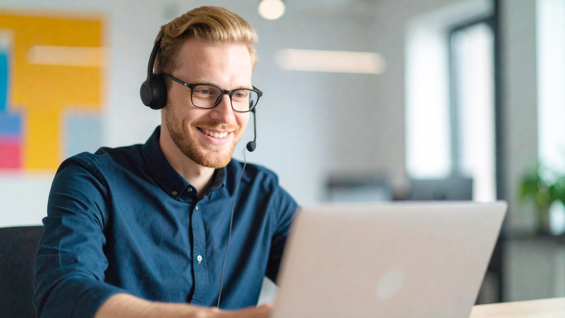 Mies kuulokkeet päässä läppärillä ottamassa osaa Suomen Yrittäjäopiston webinaarisarjaan. Tekoälykuva.