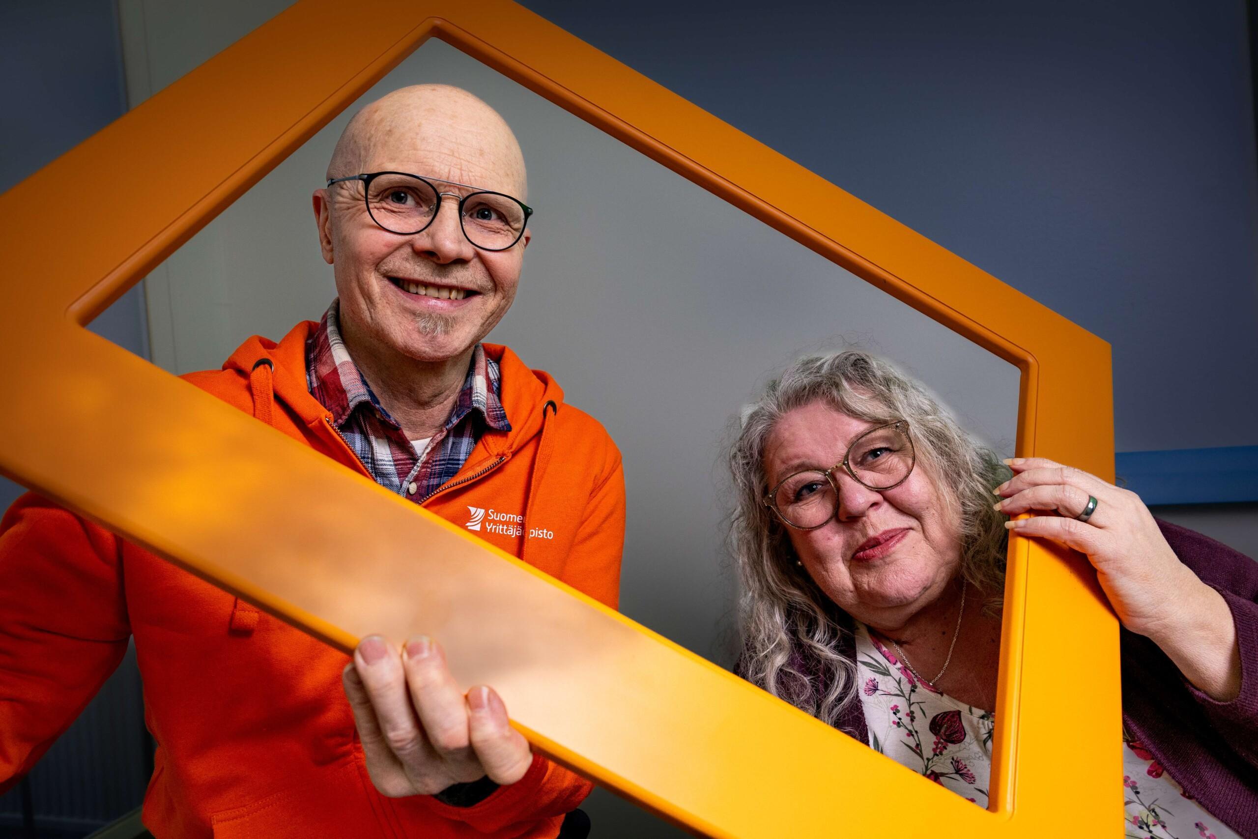 Kaksi Suomen Yrittäjäopiston kouluttajaa kurkkaavat oranssien kehyksien läpi.