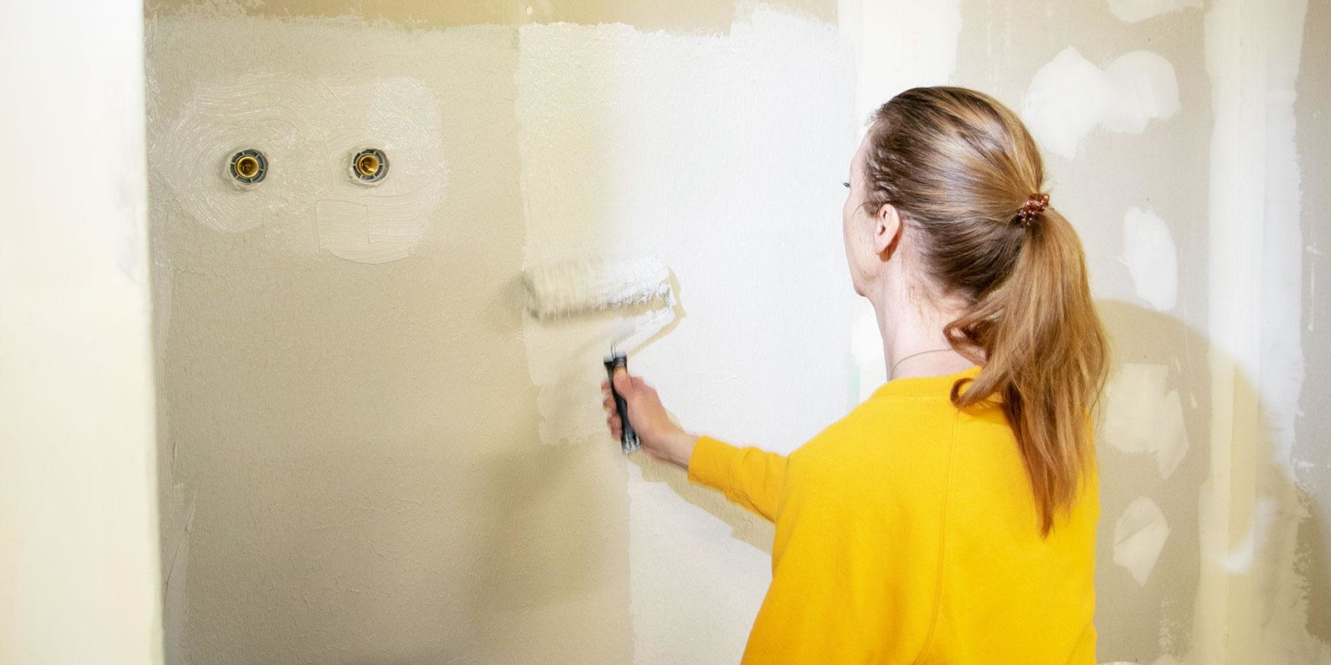 Nainen remontoi seinää, maalaa telalla seinää valkoiseksi.